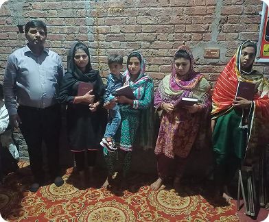 A group of people standing against a brick wall holding religous texts